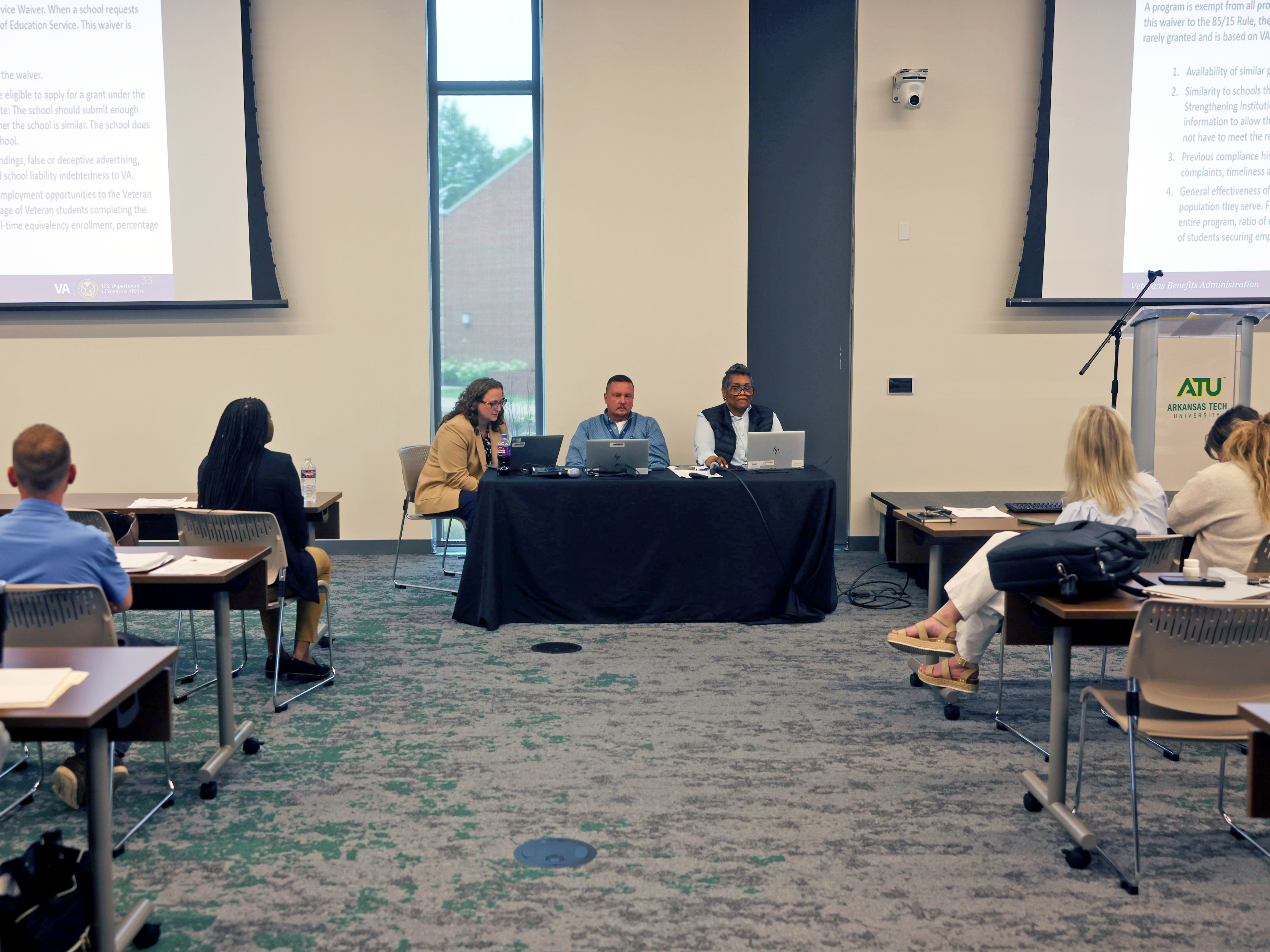 Linda Cole, Nathan Davidson, and Camisha Ragsdale sitting at a table in front of a room of school certifying officials while presenting their training. 